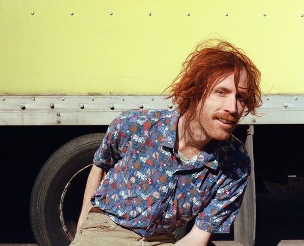 A man sits outdoors near a truck trailer