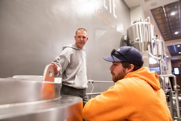 Two men talk inside of brewery.