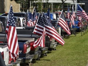 Dozens of American flags fly from a row of student vehicles.