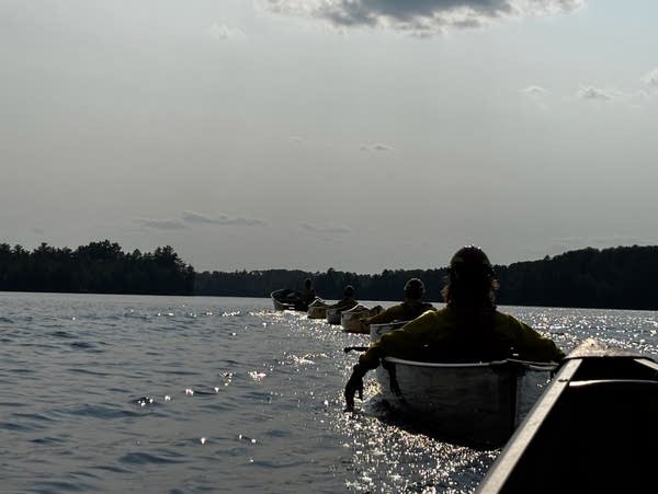 Disaster relief workers line up in their own canoes on a lake during a sunny day.