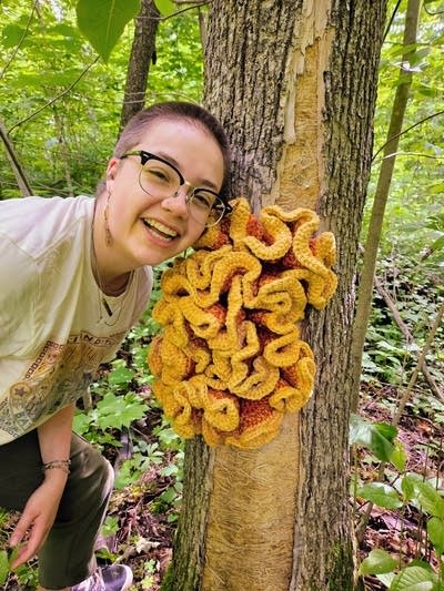 Person smiles next to crocheted musrhroom outside