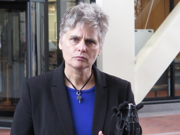 A woman in a blue shirt and jacket at a microphone.