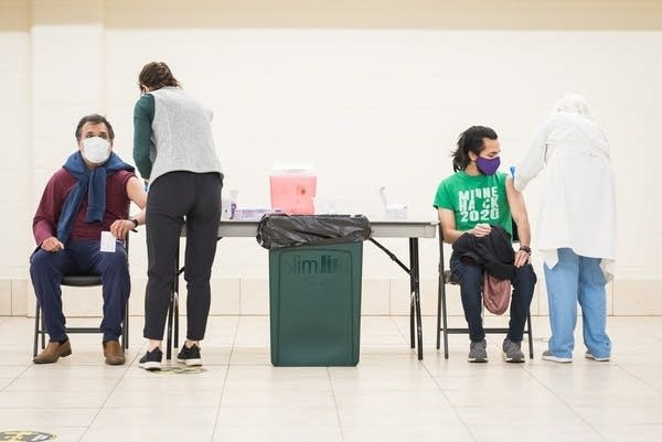 Two people sitting at tables are vaccinated. 