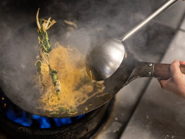 Noodles and vegetables flip in the air above a steaming wok