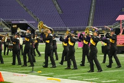 A marching band performs on the field of a football stadium.