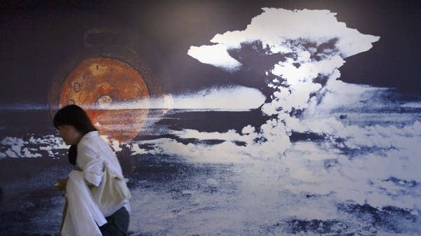 Above, a person passes a photo of the atomic bomb dropped on Hiroshima.