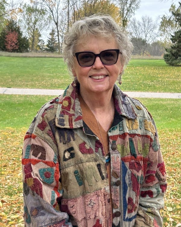 A woman in sunglasses and a multicolored jacket.