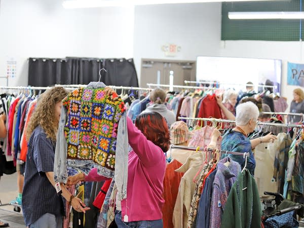 A shopper holds up a crocheted shirt in front of racks of clothing