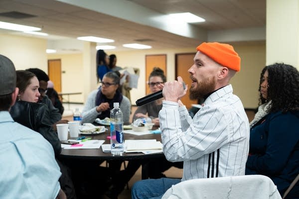 A man in an orange hat speaks into a microphone.