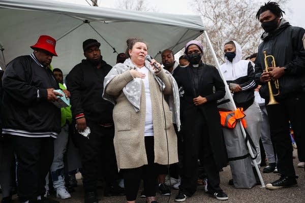 A woman cries as she speaks into a mic while others stand with her