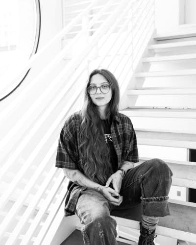 Runo Plum wears a button-down shirt over a T-shirt, jeans, and boots.