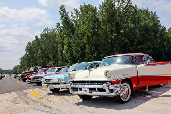 A row of classic cars is parked on a highway.