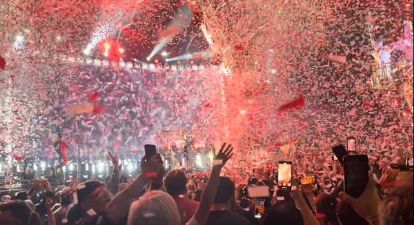 People cheer on Kiss concert while confetti filters down and lights flash.