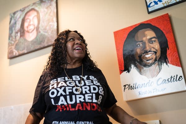 A Black woman smiles up at a painting of her son