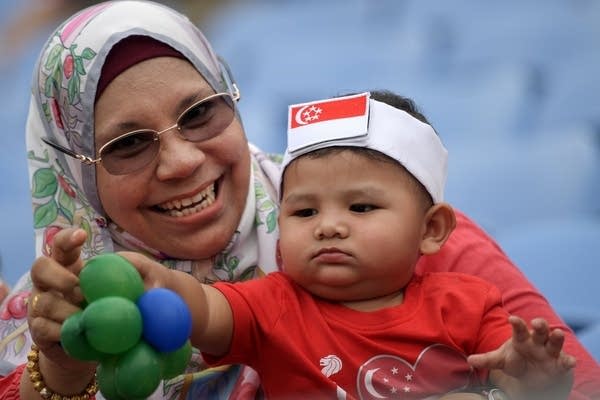 A woman holds a baby wearing a headband with the Singapore national flag as they wait for the start of the 54th National Day Parade in Singapore on August 9, 2019. 
