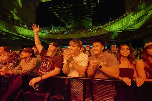 Music fans cheer and applaud an artist performing onstage in a large music venue