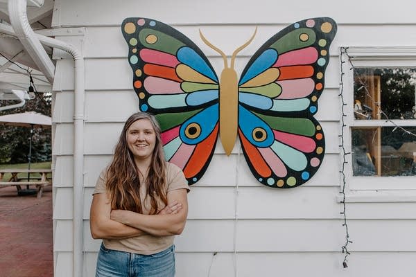 A woman stands in front of a large, colorful butterfly mounted to a house