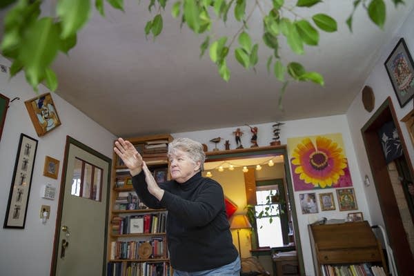 A woman practices tai chi in a room with paintings on the walls.