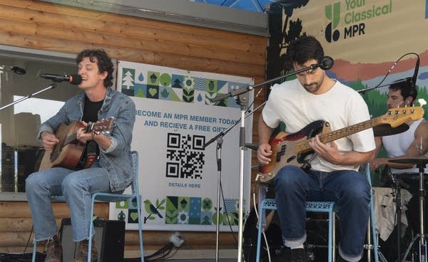 Three musicians perform on an outdoor stage at a fair