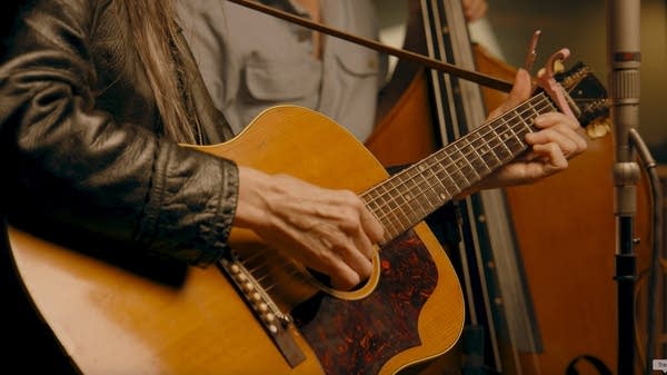 A woman sings and plays a guitar in a recording studio
