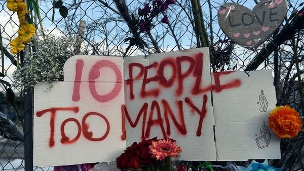 A sign reading "10 People Too Many" along with flowers hang from the perimeter fence outside a King Soopers grocery store in Boulder, Colorado on March 24, 2021, to honor the 10 people killed during a mass shooting at a King Soopers grocery store.