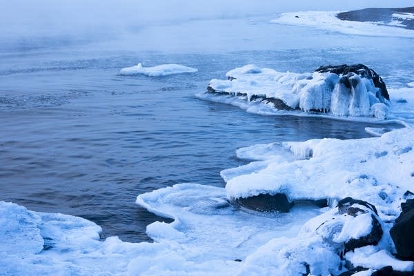ice forms over rocks next to a lake