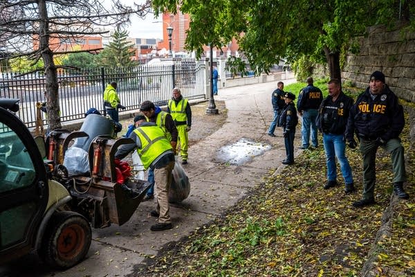 St. Paul police watch as city workers clean up trash.