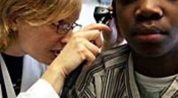 Dr. Maura Shea looks through an otoscope during an examination of patient Michelo Cineas at the Codman Square Health Center in Dorchester, Mass.