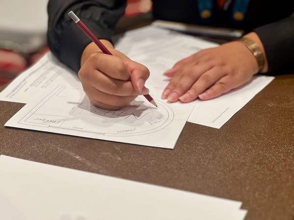 Closeup of a woman drawing an architectural design on a sheet of paper.