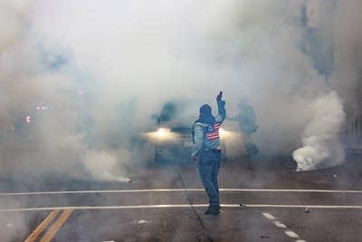 A protester raises an arm in front of a large cloud of chemical irritants.