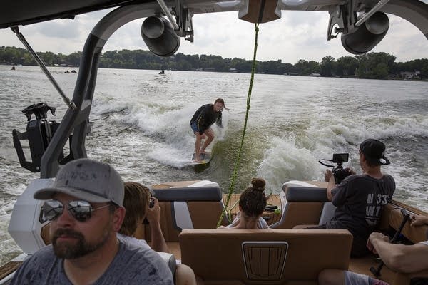 A man wakesurfs behind a boat as passengers watch. 