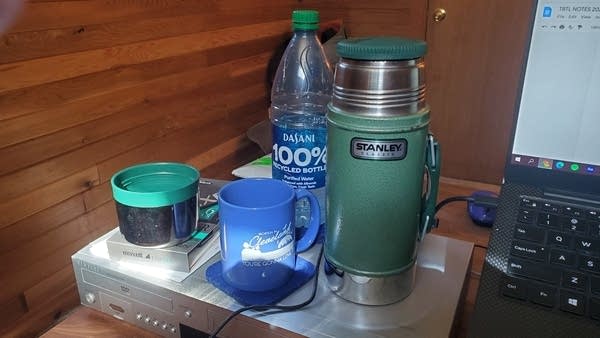 Photo of green thermos, blue coffee cup, and plastic water bottle on desk