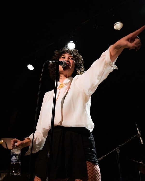 A woman sings into a microphone and points her finger