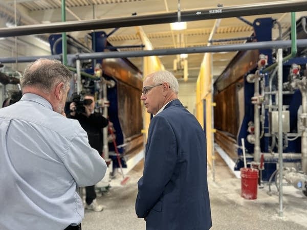 Two people stand in a room with pipes and infrastructure around them.