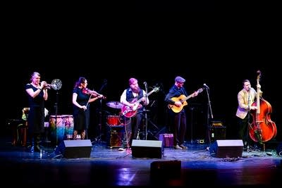 A five-piece band performing onstage in a theater