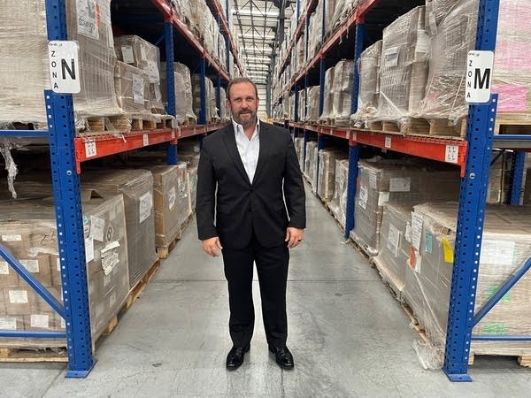 Guillermo Fernandez de Jauregui stands in a warehouse. He is flanked by industrial shelves filled with boxes.