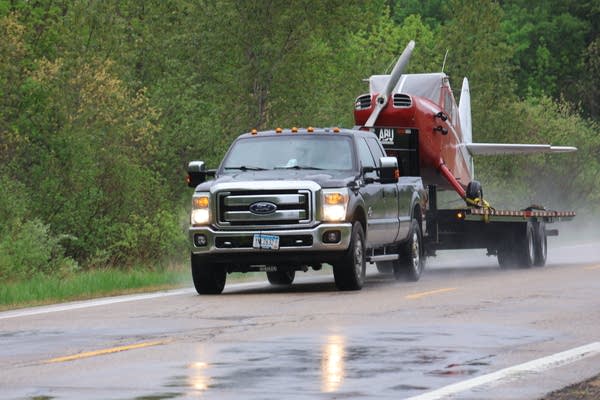 A truck hauls a red airplane with its wings removed.