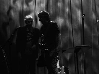 Two people stand in the shadows.