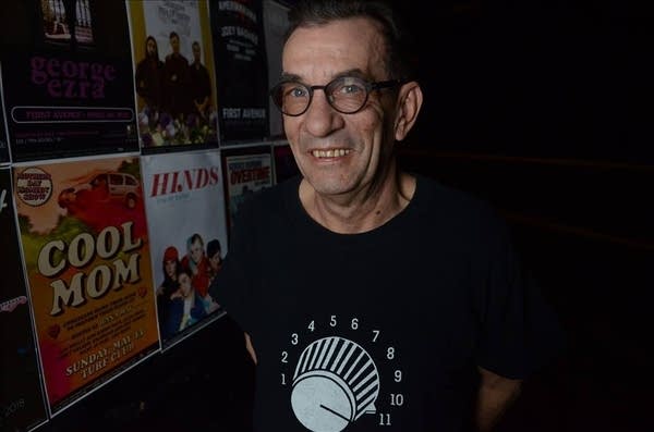 A man stands by a wall covered in band posters