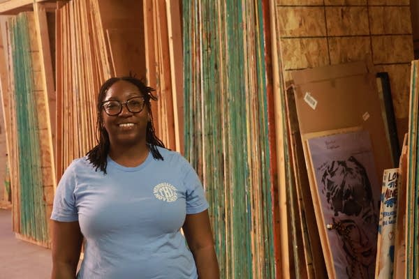 woman stands beside stacked plywood art