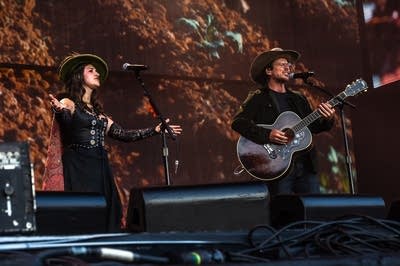 Two people in stylish hats perform on a large outdoor stage