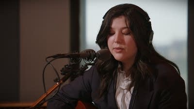 A woman sings and plays guitar in a recording studio