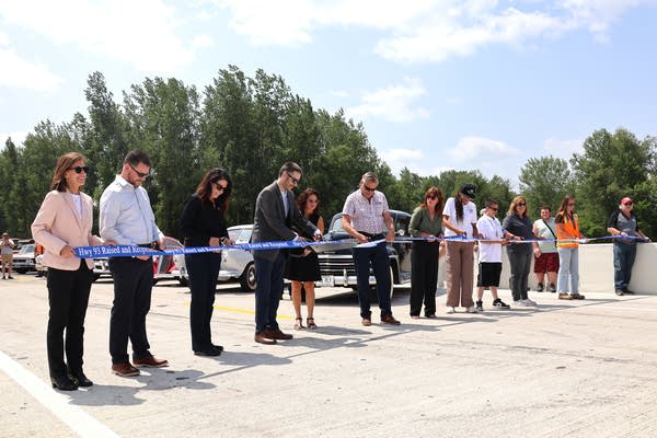A row of people lines up for a ceremonial ribbon cutting on a bridge.