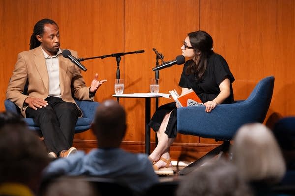Two people talk into microphones on stage. 