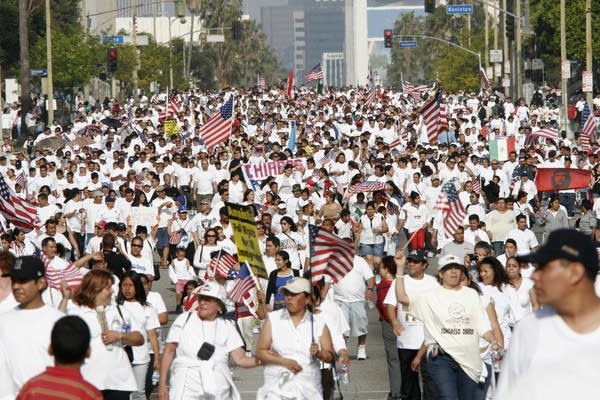Thousands of people in white march and hold signs and American flags.