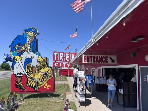 A woman stands outside a red building next to a giant pirate sign. 