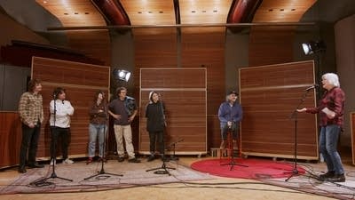 Seven people have a conversation in a recording studio