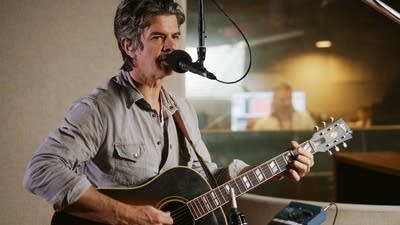 A musician sings and plays guitar in a recording studio