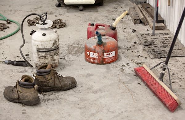 Boots, a broom and gasoline cans are among the items on a concrete floor.