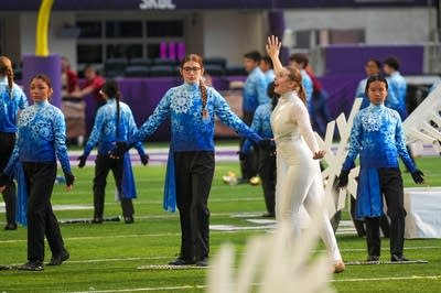 A marching band performs on the field of a football stadium.